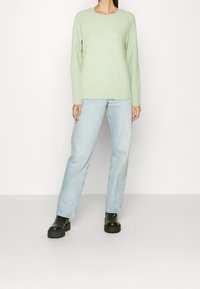 Maglione verde chiaro realizzato in materiale morbido, abbinato a jeans dritti blu chiaro e stivali neri alla caviglia chunky. Design semplice, dettagli minimi.