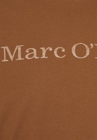 Tela de algodón marrón con una textura suave, que presenta el nombre de la marca "Marc O'" en una fuente bold de color claro.