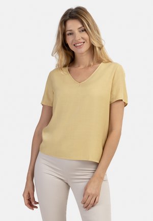Top a maniche corte, scollato a V, in un leggero giallo e tessuto morbido. Presenta una vestibilità comoda e orlo dritto. Indossato con pantaloni chiari.