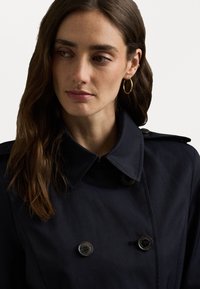 Marine trenchcoat met een dubbelgeknoopt ontwerp, grote kraag en knoopaccenten. Glad weefsel met een schone, minimalistische uitstraling.