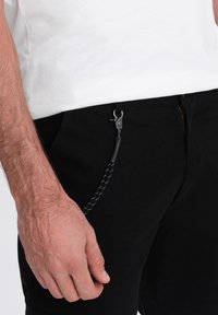 Černé kalhoty s hladkým povrchem, které mají zip a ozdobnou šňůrku s stříbrnou sponou na kapse.