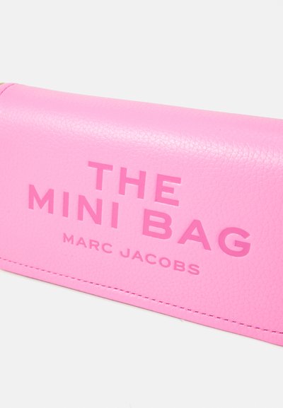 Pink leather mini bag with embossed text reading "THE MINI BAG" and "MARC JACOBS." Smooth texture and visible stitching details.