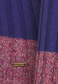 Pull en maille présentant des sections rayées violettes et rouges, avec une finition texturée et une petite étiquette logo en laiton.