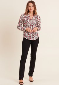 Blusa a maniche lunghe con un motivo astratto bianco, rosso e nero, abbinata a pantaloni neri aderenti e sandali neri con tacco.