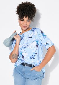 Blusa floral azul claro con mangas cortas, que presenta una variedad de flores en acuarela; combinada con jeans azul claro adornados con perlas.