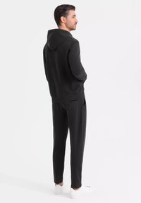 Svart hoodie och matchande joggers, tillverkade av mjukt tyg. Har en framficka och elastiska muddar, parat med vita sneakers.