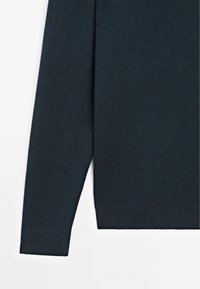 Maglione lavorato a maglia di colore blu navy scuro con scollo rotondo, maniche lunghe e polsini a coste. La texture è liscia con una finitura morbida.