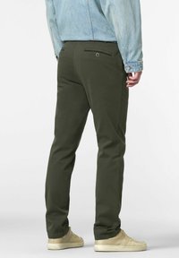 Chinos verde oliva con una vestibilità slim, dotati di tasca posteriore con chiusura a bottone, abbinati a sneaker beige e a una giacca di jeans leggera.