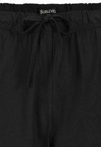 Schwarze lockere Hose mit elastischem Bund und gebundenem Zugband. Hergestellt aus leichtem Material, mit glatter Textur und einfachem Design.