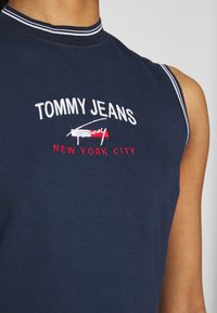 Marinblå ärmlös skjorta, i bomullsmaterial, med vit och röd broderad text "TOMMY JEANS" och "NEW YORK CITY", samt en ribbad krage.