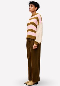 Gestrickter Pullover mit rosa, braunen und cremigen Streifen; gerippter Saum und Bündchen. Kombiniert mit hochgeschnittenen braunen Hosen und hellbraunen Schuhen.