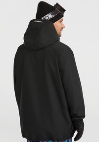 Zwarte capuchonjack met een gladde, matte afwerking, voorzien van elastische manchetten en de merknaam "ONEILL" op de achterkant. Handschoenen maken de look compleet.
