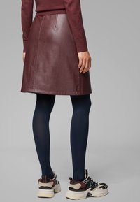 Burgundy läder A-linje kjol med en subtil lyster, ihop med marinblå strumpbyxor och tjocka svarta och beige sneakers.