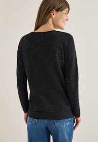 Maglione nero a maniche lunghe con un design a maglia testurizzata, scollatura rotonda e vestibilità rilassata, abbinato a jeans blu.
