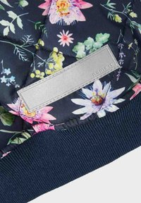 Bloemen-gebloemde quilted jas met een marineblauwe achtergrond. Beschikt over felgekleurde bloemen, geribbelde marineblauwe manchetten en een rechthoekig zilverkleurig label.