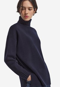 Mörkblå polotröja med ribbad detaljering vid kragen och fållen. Mjuk textur, sänkta axlar och synliga sidofickor.