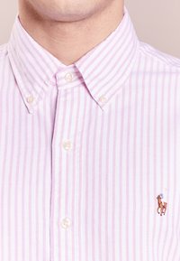 Ljusrosa och vit randig skjorta med knapp-utfällning, med en liten broderad hästlogga på bröstet och pärlknappar.