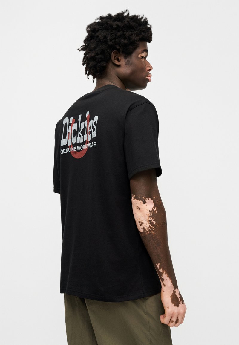 Black cotton t-shirt with short sleeves, featuring a large printed logo on the back in white and red. Solid color, relaxed fit.