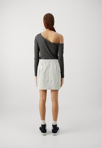 Haut gris asymétrique à manches longues, associé à une mini-jupe blanche à rayures, avec des poches latérales. Baskets noires avec des accents blancs.