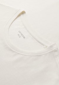 Bílý bavlněný tričko s kulatým výstřihem a krátkými rukávy, s měkkou strukturou a jednoduchým designem. Značka je viditelná uvnitř výstřihu.