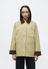 Beige arbejdsjakke med brun fløjlskrave og manchetter, med to forlommer og en firkantet pasform. Tekstureret stof med en glat finish.