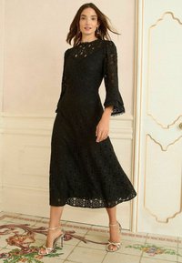 Mustmustest musta, millel on keha lähedane ülaosa, flared varrukad ja lillelised lõikemustritega, koos hõbedaste rihmadega kontsadega.