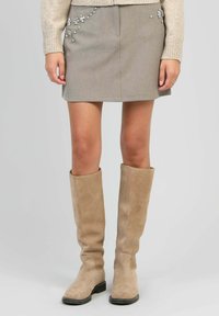 Jupe mini grise avec des éléments floraux décoratifs, associée à des bottes en suède beige jusqu'aux genoux, dotées d'un talon bloc et d'une texture lisse.