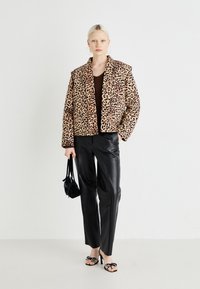 Korte jakke med leopardmønster i mykt stoff, brukt over en brun topp, kombinert med svarte bukser i kunstlær og svarte hæler.