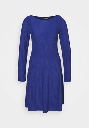 Sininen ribattu mekko, jossa on pitkät hihat ja avara kaula-aukko. Mekossa on istuva yläosa ja leveä helma, joka on valmistettu teksturoidusta neulekankaasta.