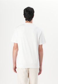 Camiseta blanca de manga corta con cuello redondo, hecha de algodón, que presenta una textura suave y un ajuste relajado, vista desde la parte trasera.