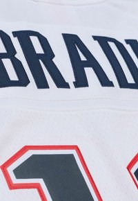 Weißes Sporttrikot mit marineblauen, gestickten Schriftzug "BRADY" über einer rot akzentuierten Nummer "12". Der Stoff hat ein Netzmuster.