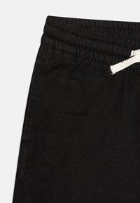 Pantalons de jogging noirs en tissu texturé, avec une taille élastique et un cordon blanc. Comprend une poche latérale pour plus de commodité.