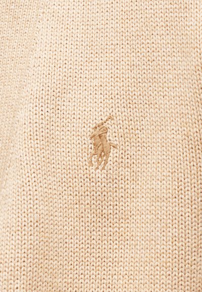 Μπεζ πλεκτό πουλόβερ με υφή και μικρό, κεντημένο λογότυπο σε ελαφρώς πιο σκούρο μπεζ στο μπροστινό μέρος.