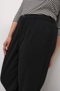 Un pantalon large noir en tissu doux avec une taille haute, des plis avant et des poches latérales, associé à un haut rayé.
