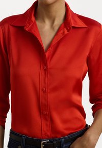 Camisa de botão em cetim vermelho com colarinho spread, mangas longas e textura suave. Fechada com botões do mesmo tom na frente.