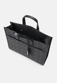 Sac cabas noir avec une finition texturée et des accessoires en argent. Il présente un motif monogramme MK, deux poignées et une poche intérieure zippée.