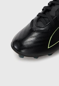 Scarpini da calcio neri con upper in sintetico testurizzato, presentano una punta liscia, lacci neri e un logo verde chiaro a contrasto sul lato.