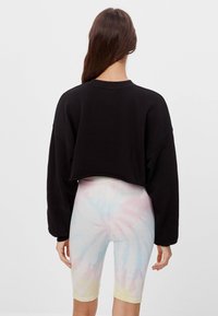 Svart kort sweatshirt med långa, lösa ärmar, i kombination med pastellfärgade tie-dye ribbade cykelbyxor. Mjuka texturer och avslappnad passform är synliga.
