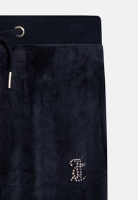 Jūras spēku velūra sporta bikses ar ribotu vidukli, zelta auklu un rhinestones logo akcentu kreisajā apakšējā pusē. Mīksta tekstūra, brīva piegriezuma valkāšana.