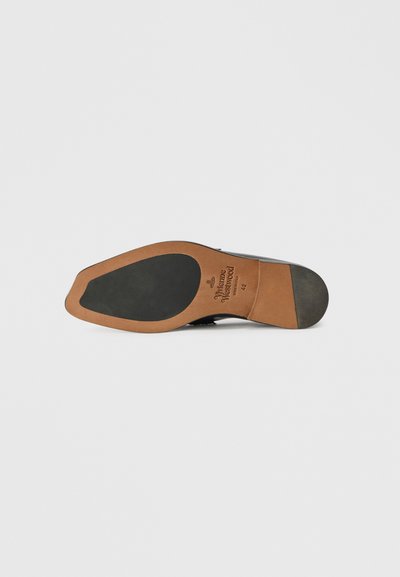 Sola de sapato de couro preto com um destaque em borracha tan, textura suave e detalhe de logotipo em relevo. Bico arredondado e design plano.