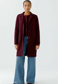 Burgundy wool coat with a notched collar and button closure, paired with a ribbed maroon sweater and wide-leg blue jeans.
