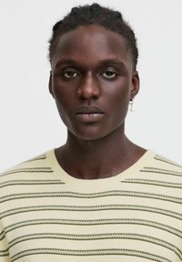 Light yellow striped sweater featuring horizontal green and white stripes, ribbed neckline, and smooth knit texture.