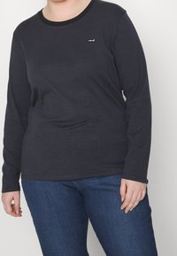 Sinih raitipaita pitkillä hihoilla, valmistettu puuvillasta ja pyöreällä kaula-aukolla, jossa on pieni Levi's-logo rinnassa. Yhdistetty sinisiin farkkuihin.