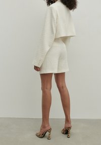 Kaksiosaista vaaleankreemiväriä, joka koostuu lyhyestä takista ja shortseista, yhdistetty leopardikuosisisiin korkokenkiin. Neutraali tausta.