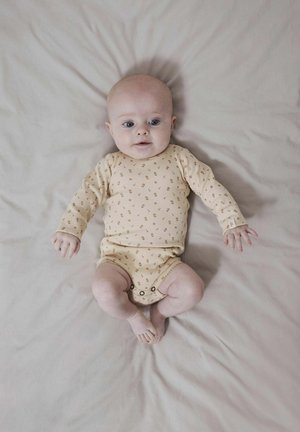 Heled kreemja ribadega bodi, millel on väikesed pruunid lillemustid, pika varrukaga ja all nupuga kinnitamine, mida kannab beebi, kes lamab neutraalsel pinnal.