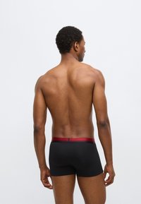 Boxer noir avec une ceinture élastique rouge, présentant une texture lisse et une coupe ajustée, vu de dos.