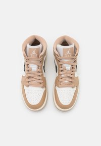 Paire de baskets montantes Nike Air Jordan beige et blanches avec lacets noués, vue de dessus sur fond blanc.