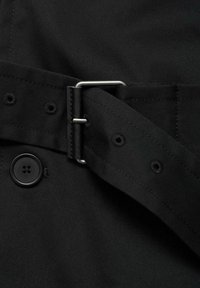 Tela negra con un botón y un cinturón que cuenta con una hebilla de metal plateado y agujeros. Textura suave y diseño aerodinámico.