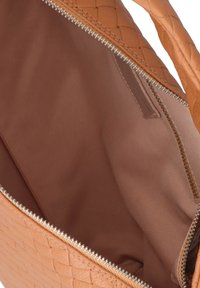 Sac fourre-tout en cuir tressé beige avec une doublure intérieure lisse et une fermeture éclair argentée. Aucun compartiment extérieur visible.