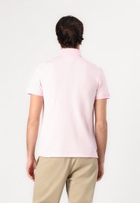 Polo de manga corta en rosa claro, confeccionado en algodón suave. Presenta un cuello clásico y un dobladillo recto con un sutil detalle de costura en la parte posterior.